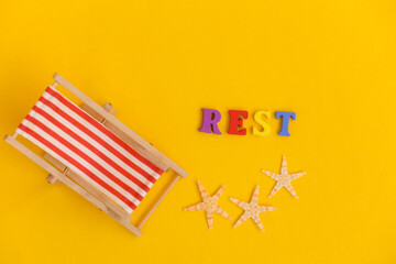 Mini beach deck chair and starfish on yellow background. Word rest. Symbol of beach holidays, resort.  Relax, Summer minimal concept. Top view