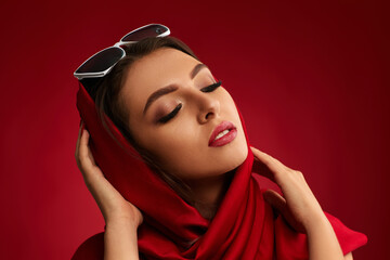 Portrait of beautiful brunette sexy girl with luxurious make-up in bright red headscarf on red...