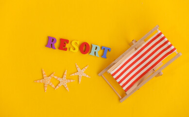 Fototapeta na wymiar Mini beach deck chair and starfish on yellow background. Word resort. Symbol of beach holidays, resort. Relax, Summer minimal concept. Top view