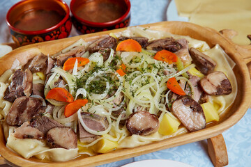 Nationally Kazakh dish beshbarkak in wooden utensils. On white table. Close-up