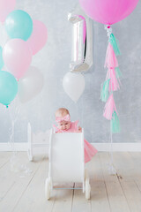 Girl in a pink dress and balloons celebrates her first birthday