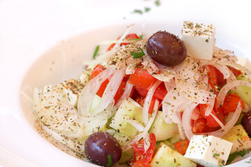 Fresh spring salad with tomato, cucumber, onion, black olives, feta cheese, olive oil, sprinkled with herbs, served on white plate with copy space.