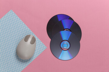 Old-fashioned retro CD's and pc mouse on pink blue pastel background. Top view