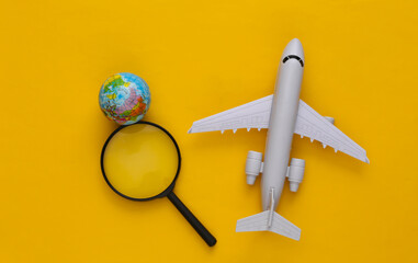 Travel concept. Airplane, magnifier with a globe on yellow background. Top view. Flat lay