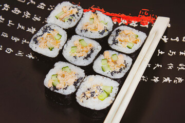 Sushi rolls with salmon and cucumber on a plate with chopsticks next to it.
