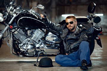 Cool man biker in sunglasses sitting near his motocycle