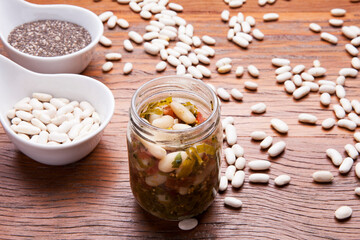 Nutrition concept - Healthy meal of white beans, chia and vegetables in glass jar over wooden background. Glass cup on wood table, benefits for diet, weight control and diabetes