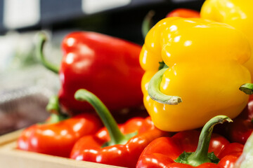 Side view of yellow bell pepper lying on red peppers on the shelf. Close-up of fresh agricultural vegetables in grocery. Vegeterian food, dieting, healthy eating.