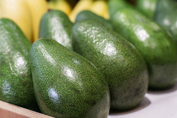 Green avocado on grocery shelf. Close-up of vitamin healthy fruits in supermarket. Fresh organic food, healthy eating, seasonal vitamins.