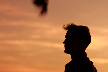 Close up head shot silhouette young caucasian man with side view against sunset sky, summer...