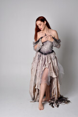 full length portrait of girl wearing old, torn wedding dress. standing pose on a studio background.