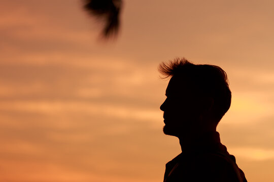 Close up head shot silhouette young caucasian man with side view against sunset sky, summer vacation lifestyle