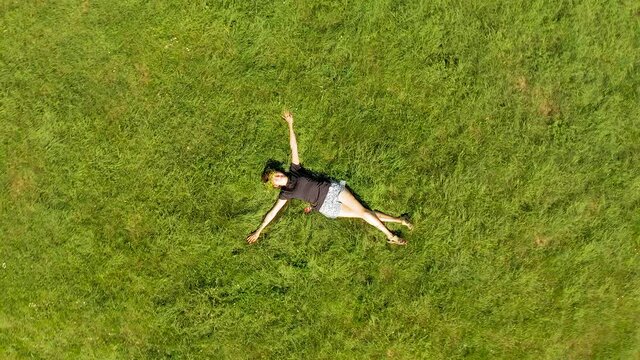 Drone fly out from a girl lying on grass of a green meadow with panoramic view to the surrounding nature of Heidi Land in Switzerland's Alps mountains
