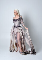 full length portrait of blonde girl wearing long torn, old wedding gown. standing pose on a studio...