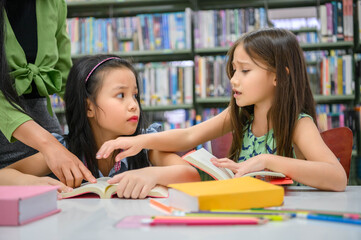 Two cute girls conflict while reading books in library when teacher teaching