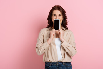 Obraz premium Brunette woman showing smartphone with blank screen near face on pink background