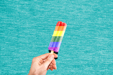 Hand holding ice cream with LGTBI colors on turquoise background