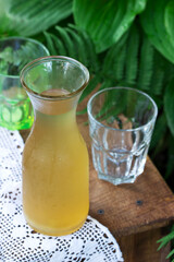 Rhubarb compote in a transparent jug and glasses on a wooden chair in the garden.