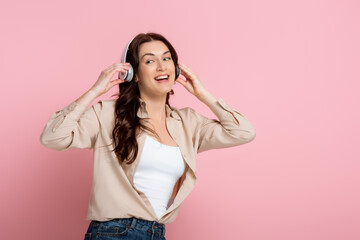 Cheerful woman in headphones looking away on pink background