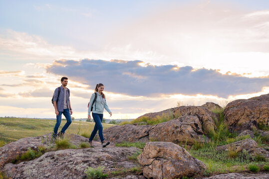 Young Happy Travelers Hiking with Backpacks on the Rocky Trail at Summer Sunset. Family Travel and Adventure Concept.