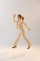 Fototapeta premium Side view of woman in formal wear jumping on grey background