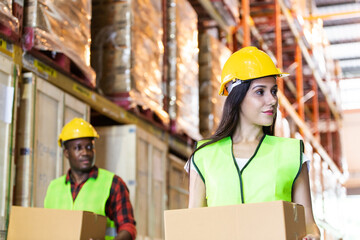 Caucasian woman and African American man worker carry box in factory warehouse. Export import or logistics service business, shipping delivery and employee people concept