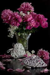 Stillleben mit Pfingstrosen und dekorativen Herzen auf schwarzem Hintergrund