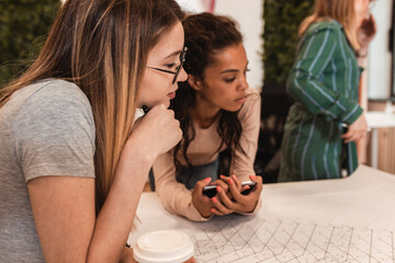 Group of modern young business women in casual wear discussing architectural designs in the creative office.