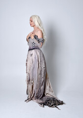 full length portrait of blonde girl wearing long torn, old wedding gown. standing pose on a studio background.