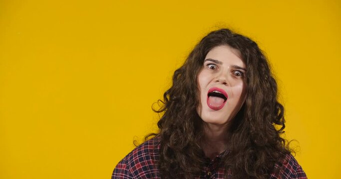 Close-up attractive plus-size model posing. A curly-haired brunette on a bright yellow studio background demonstrating different emotions. Girl flirting, making freaky faces and showing tongue