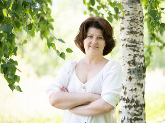 Russian woman with arms crossed near the birch in the summer