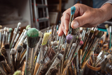 A hand grasping one of many paintbrushes
