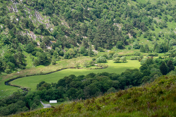 Fototapeta na wymiar Wicklow Mountains Road. This place is famous for uncontaminated nature, misty landscapes and lakes. Typical Irish farms in background. Panoramic view during summer time