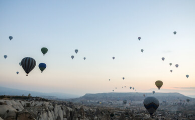 Colorful hot air balloons flying over rock and valley landscape in morning fog at sunrise in Cappadocia, Anatolia, Turkey