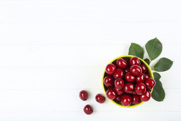 Sweet cherries in bowl with green leafs on white wooden table