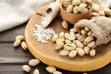 Tasty pistachios in sack, bowl and scoop with salt on wooden table