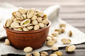 Tasty pistachios in bowl with napkin on wooden table