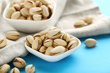 Tasty pistachios in bowls with napkin on blue background