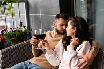 handsome man hugging beautiful woman and clinking glasses of red wine outside
