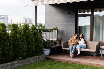 handsome man and happy woman sitting on outdoor sofa and holding wine glasses