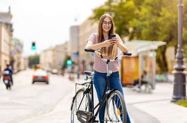 Fototapeta na wymiar Attractive young woman using smartphone while out cycling through the city 