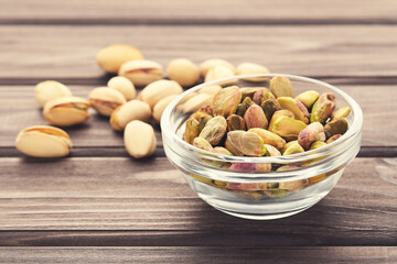 Tasty pistachios in glass bowl on wooden table