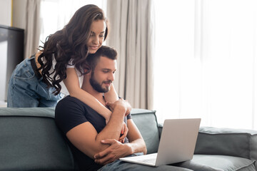 Fototapeta na wymiar happy girl hugging handsome boyfriend using laptop in living room