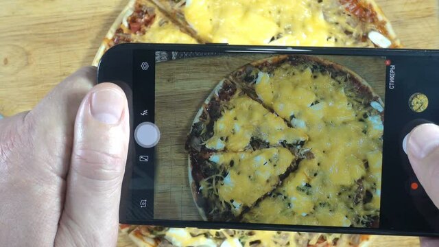 4K view of hands holding a smartphone and taking sliced pizza photos. Close-up