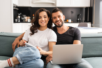 happy young couple looking at camera and holding gadgets