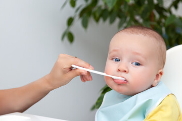 First feeding of baby boy, eat yoghurt, dirty mouth, holds spoon