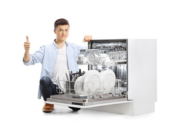 Teenager kneeling next to a dishwasher and showing thumbs up