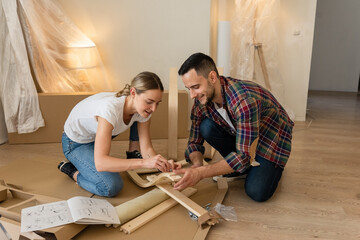 Happy Smiling Couple Collects Furniture as a Team. Girl Helps to Assemble Chair Details. Moving to New Apartment, Young Family Assemble Furniture