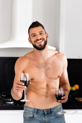 happy and shirtless man holding glasses with red wine