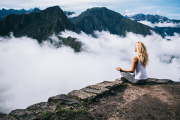 Calm and inspiration on peak with Machu Picchu, relaxed woman tourist sitting in lotus pose and...